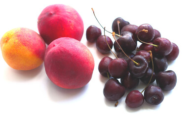 three peaches, nectarine and a handful of sweet cherries lie on a white background. Isolate, a natural dessert made from berries. A tasty, healthy snack, a piece of summer, a harvest. Fruit on a white