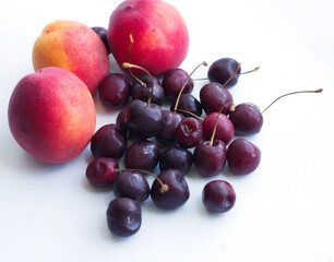 three peaches, nectarine and a handful of sweet cherries lie on a white background. Isolate, a natural dessert made from berries. A tasty, healthy snack, a piece of summer, a harvest. Fruit on a white
