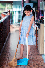 Smile asian little girl sweeping with broom and dustpan in the house