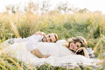 Family in a field. Happy pregnancy and motherhood concept. Pregnant woman and her handsome man lying together on checkered plaid, outdoor in beautiful summer field