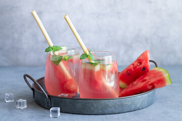 Summer cold drink with watermelon, mint leaves and ice on a vintage tray. Two glasses with bamboo eco straws