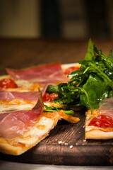 pizza with Parma ham and arugula on a wooden stand