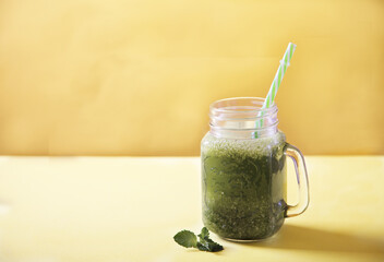 Fresh green smoothie in a mug jar and a mint leaf on a yellow background. Copy spaes.
