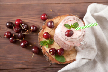 Milk and cherry smoothies in a glass mug jar, next to a cherry, a linen napkin on a wooden stand. Flat lay