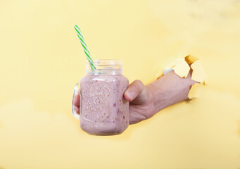 A man's hand holds a fresh smoothie made from milk and cherries in a glass jar on a yellow background. Copy spaes.