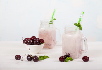 Sweet cherries and milk smoothies in two glass jars with a straw and sweet cherries in a cup, sweet cherries are scattered on the table on a concrete background.