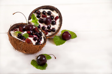 Whipped cream dessert with cherries and currants and mint leaves in coconut halves on a white plate. Summer keto dessert. Copy spaes