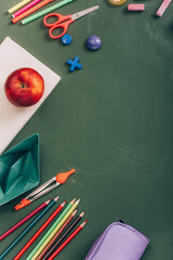 top view of ripe apple on book, paper boat and school supplies on green chalkboard