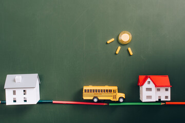 top view of house models, toy school bus on road, made of color pencils, and sun made of magnets on...