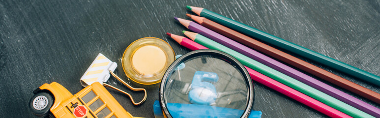 high angle view of magnifier, color pencils and school supplies on black chalkboard, panoramic shot