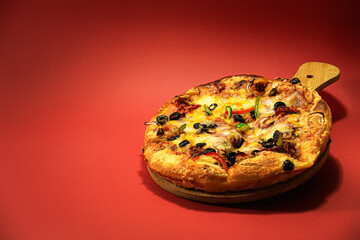 Delicious pizza with mozzarella cheese, vegetables, meat and tomatoes, isolated on red background, with available copy space.
