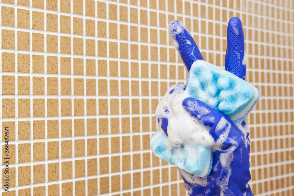 Wall mural Hand in blue glove two thumbs up with a blue sponge with foam on background of brown tiles