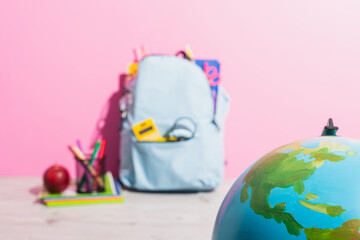 Selective focus of globe near backpack packed with school stationery, pen holder and ripe apple
