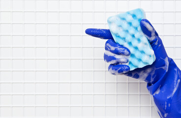 Hand in blue glove finger with blue sponge in the foam on a background of white tiles