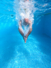 Older man dives into the blue water pool during the summer holidays.