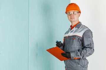 A male engineer, a construction worker in a protective helmet and glasses writes to a tablet. The...