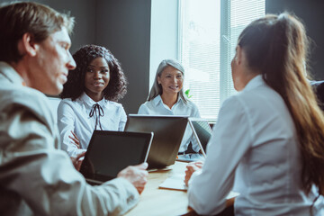 Funny business meeting of diverse team. Happy Multiethnic group of people have conversation sitting at office desk and using computers. Tinted image.