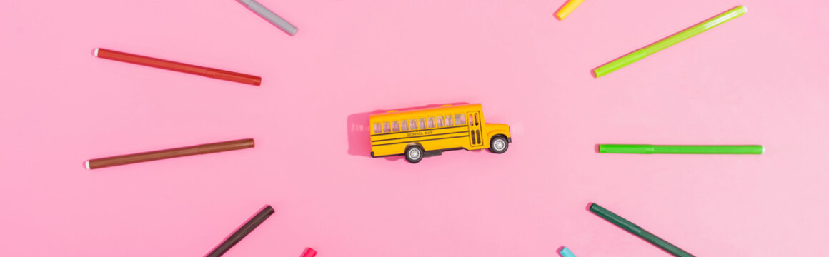 Top view of school bus model framed with color felt tip pens on pink, horizontal image