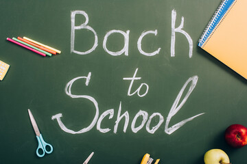 top view of back to school lettering near apples and school supplies on green chalkboard