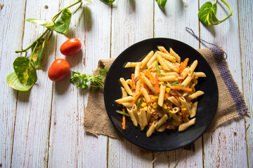 Pasta and stir fried vegetables on a black plate on a background with use of selective focus.
