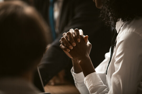 African-american businesswoman folded hands to pray for business. Dark-skinned young woman folded hands together graceful hands in foreground. Tinted image.