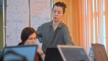 woman staff worker helps intern architect coworker gives advice tells irrl. information feedback. advise when working with ux design blueprint on computer. concept whiteboard