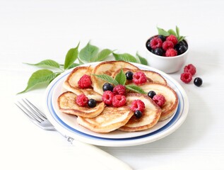 Pancakes with fresh raspberries and black currant on a plate on a white background