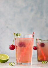 Lemonade or non-alcohol cocktail with cherry and lime in glass on grey background. Summer berry drink.