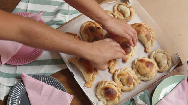 Traditional homemade rustic baked argentinian empanadas pie with vegan meat in cardboard box. Hands take pie, Fast food to go. Bakery delivery menu.
