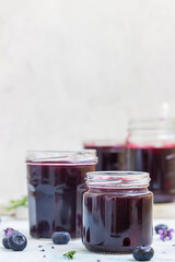 Fresh homemade blueberry, lavender and rosemary jam in glass jars on light blue background.