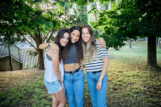 Portrait of a group of young millennials friends in a park at sunset embraced together - Beautiful women looking the camera and smiling