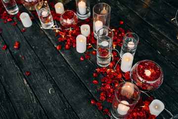 Romantic evening concept. White candles in glass vases on a wooden floor with red roses petals, outdoors. Valentine's day.