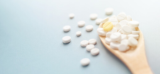 White tablets on one yellow in wooden spoon on blue background.