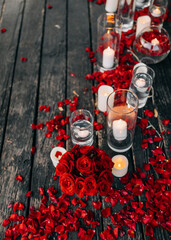 Romantic evening concept. Candles in glass vases on a wooden floor with red roses petals, outdoors.