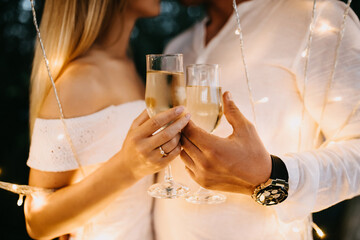 Close up of man and woman hands holding glasses of champagne, with a diamond engagement ring on woman's finger. Engagement concept.