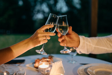 Close up of man and woman hands holding glasses of champagne, with a diamond engagement ring on woman's finger, having dinner. Engagement concept.