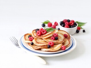 Pancakes with fresh raspberries and black currant on a plate on a white background