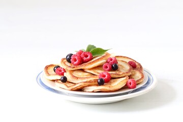 Pancakes with fresh raspberries and black currant on a plate on a white background