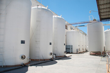 Wine processing and storage silos in winery. White cylindrical tanks with wine in a business in Salta, Argentina. Industrial barrels outside with blue sky.