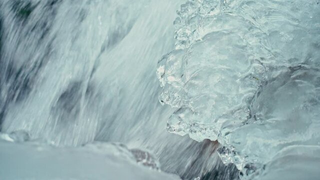 Mountain river with clear ice water with a waterfall in winter, icicles on rocks