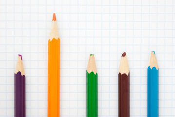 sharp  orange  pencil and colored blunt pencils on a writing-book leaf.