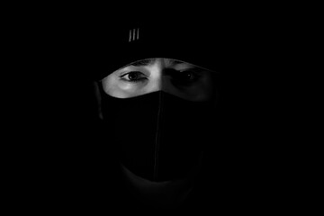 A man in a black mask and a cap. The eyes of a man in the dark
