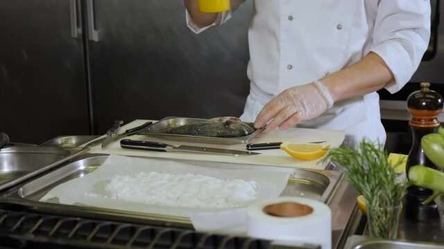 The chef pours olive oil on the fish before cooking. The process of cooking Dorado fish in a professional kitchen. Slow motion.