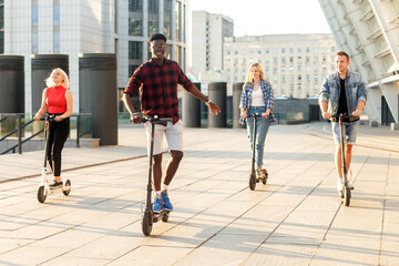 interracial group of friends ride electric scooters in the city, multiracial youth use electric vehicles © Богдан Маліцький
