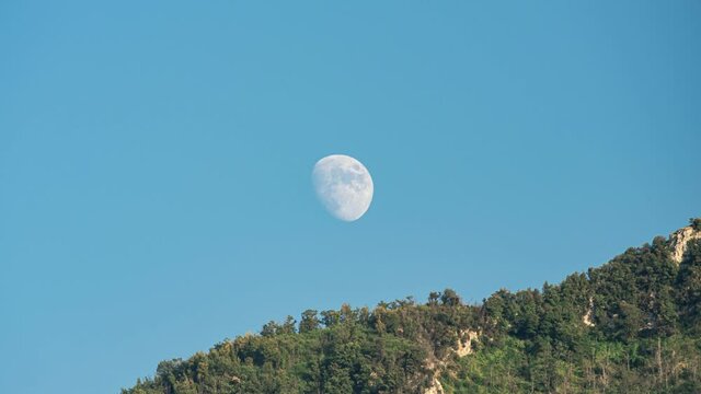 Angri, Italy. July 30th, 2020. Rising Waxing Gibbous Moon rises from behind the ridge of Mount Taccaro and continues along the line of the mountain ridge while remaining partly hidden at times.
