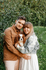 Naklejka na ściany i meble young happy couple standing near trees in the park and holding a dog