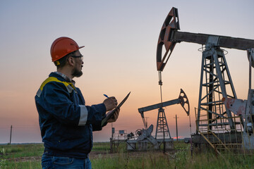 Oil worker checks an oil rig at sunset. Maintenance of oil pump jacks
