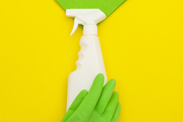 Green glove, microfiber and spray cleaner on a yellow background, top view.