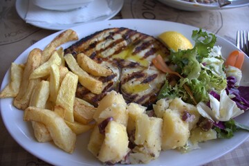 Food on a plate fish sword grilled french fries potatoes salad lemon olive oil in a cafe on the table