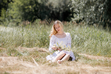 Naklejka na ściany i meble Young white woman with blondy hair dressed in a white dress in summer in a field